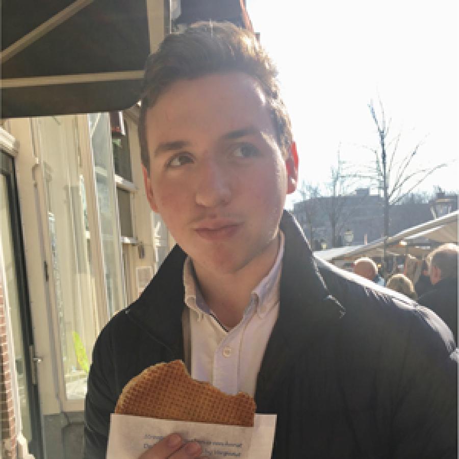 student with short hair, white shirt, jacket, holding a waffle