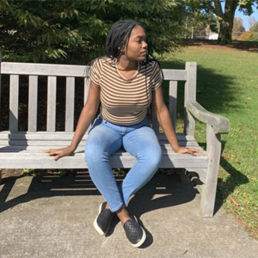 Student sitting on tan bench with trees in background