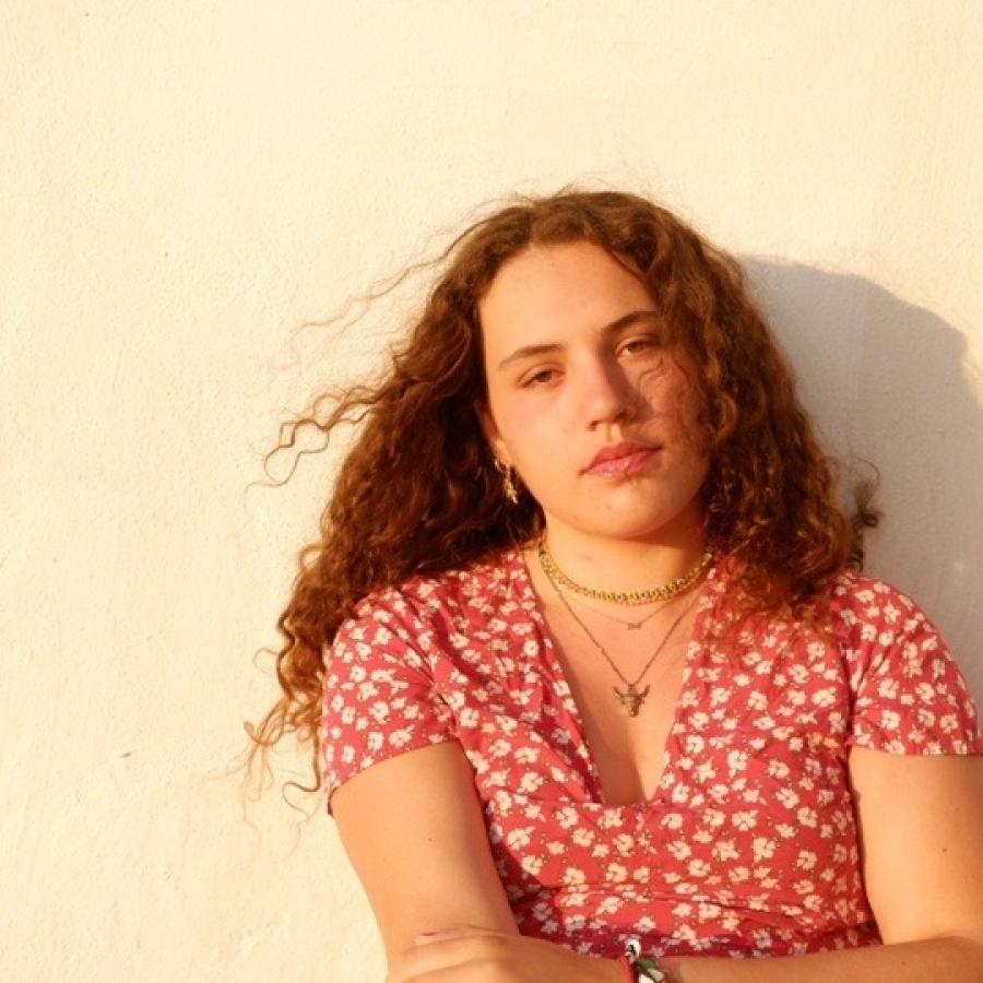 headshot of a woman leaning against a cream colored wall with arms folded.