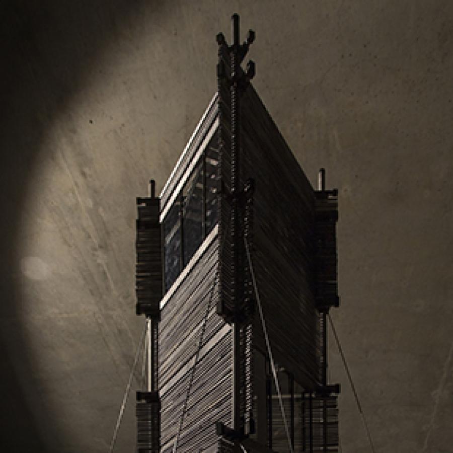 Photograph of highly detailed wooden model of tower from a low angle with a concrete ceiling as the background.