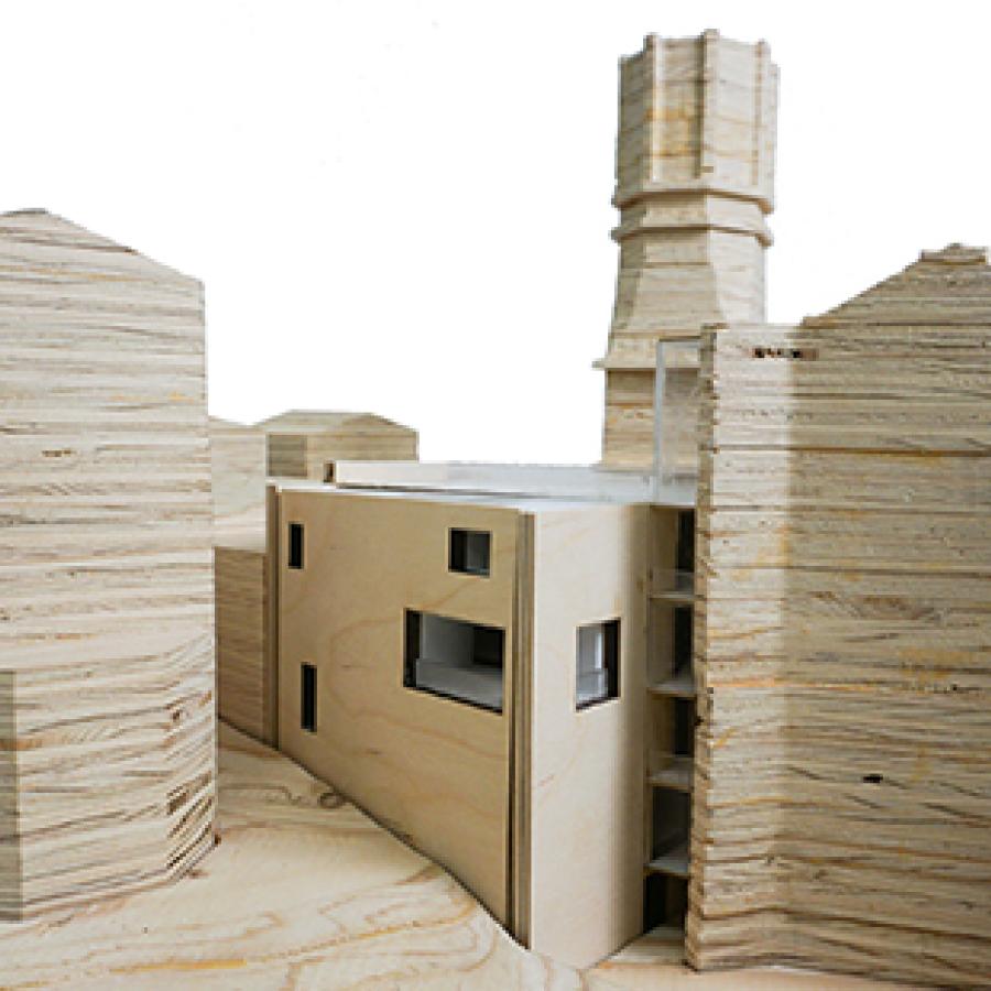 Photograph of model with site, including buildings, made of stacked plywood cut to shape, and with the project proposal made of thinner boards with rectangular perforations on the walls and white material on the inside.
