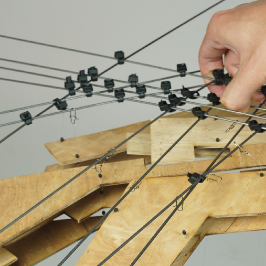 A architecture model made of plywood and piano wires held by hand.