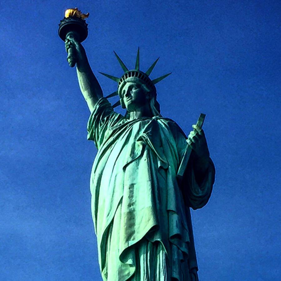 a giant green statue carrying a torch with a blue sky behind it