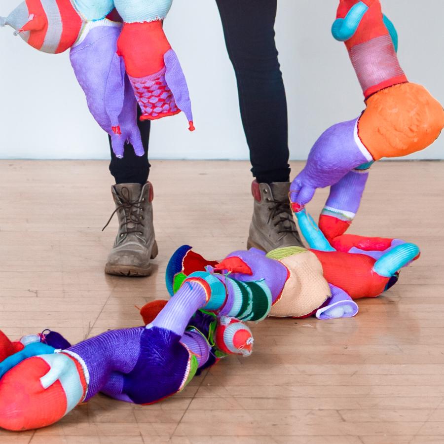 Abstract bright colorful fabric shapes draped across someone wearing black leggings and gray boots.