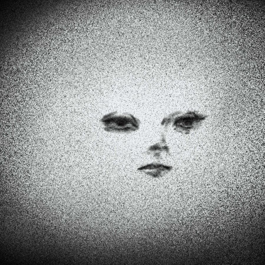 Black and grey image of feminine facial features (eyes, nose, and mouth) imposed over a grainy grey oval and black background