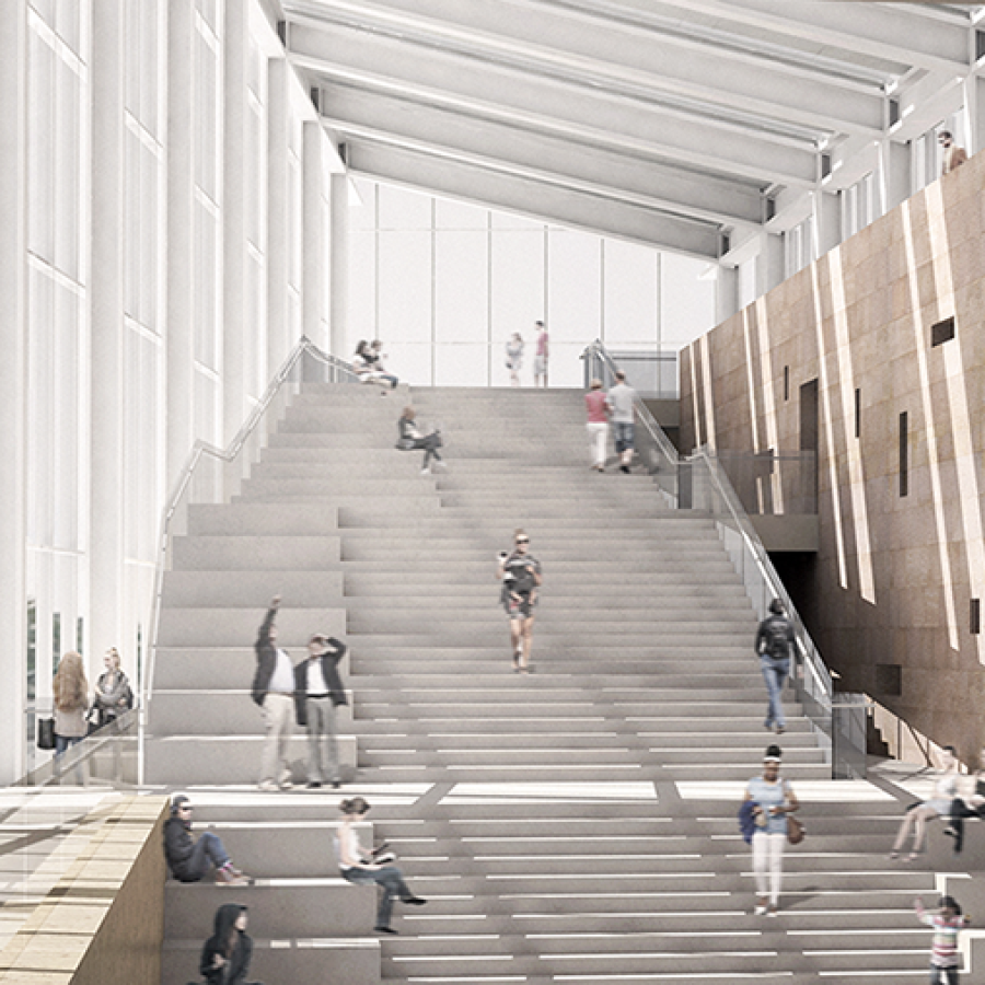 A large, open interior of a modern building, whose center consists of a large ascending staircase adjacent to a series of windows. 