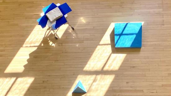 Three abstract art pieces in blue hues on a wooden floor, looking at them from above.
