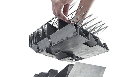 Photograph of hand placing top half of model made from thin-plate bended and welded steel onto bottom half of model.