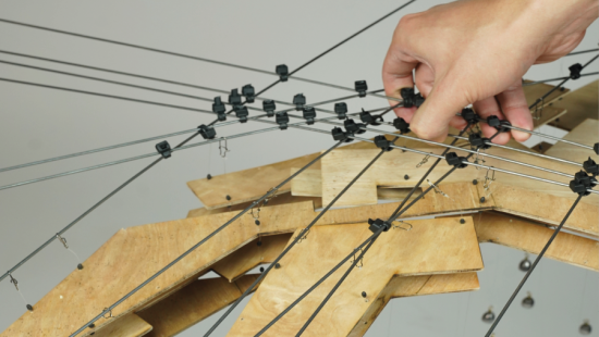 A architecture model made of plywood and piano wires held by hand.