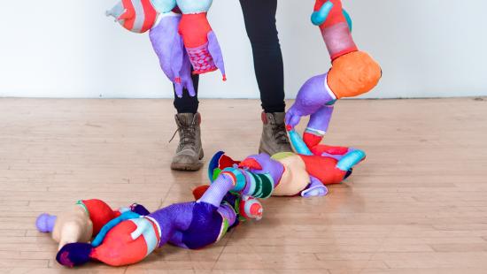Abstract bright colorful fabric shapes draped across someone wearing black leggings and gray boots.