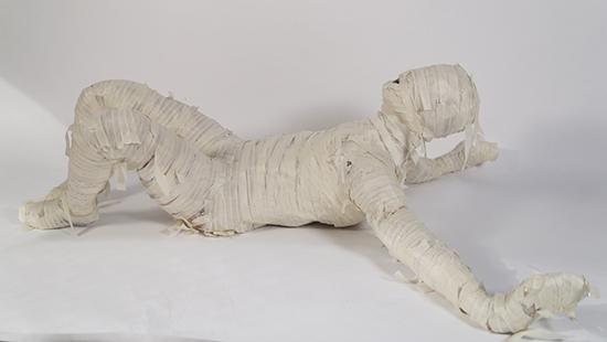 sculpture of a person lying on the ground wrapped in masking tape.