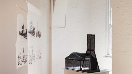 Two white banners with four black images printed on them hanging next to a black transparent building model in a white room.