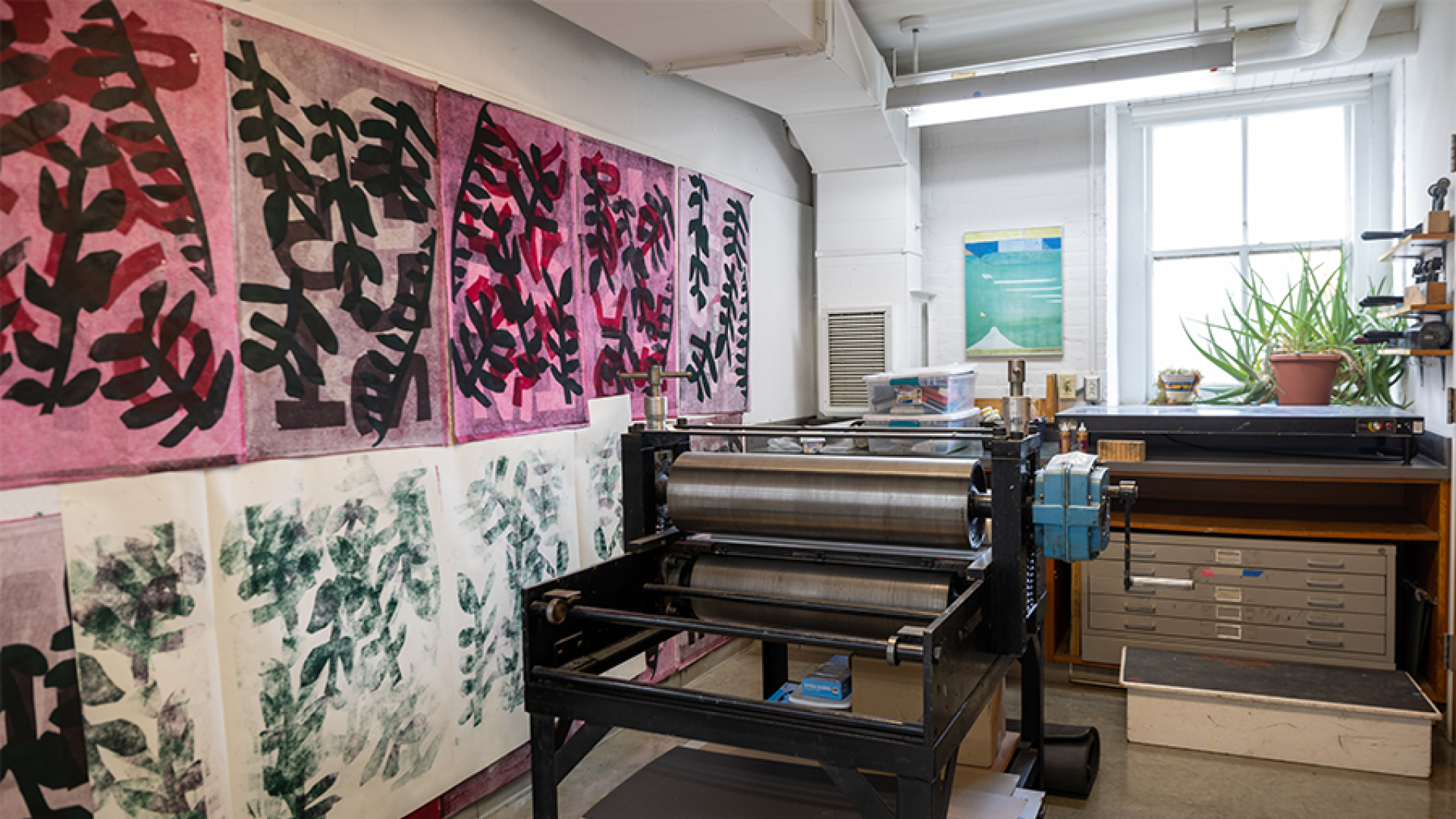 A room with artwork hung on the wall and a large press machine.