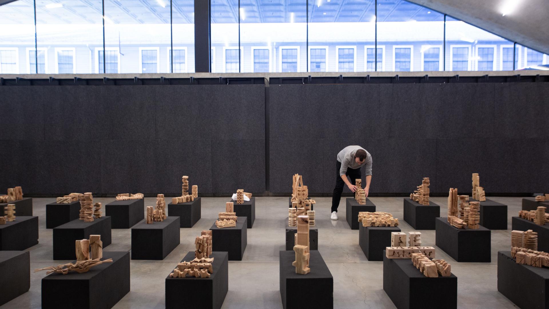 A person setting up architectural models on black pedestals.