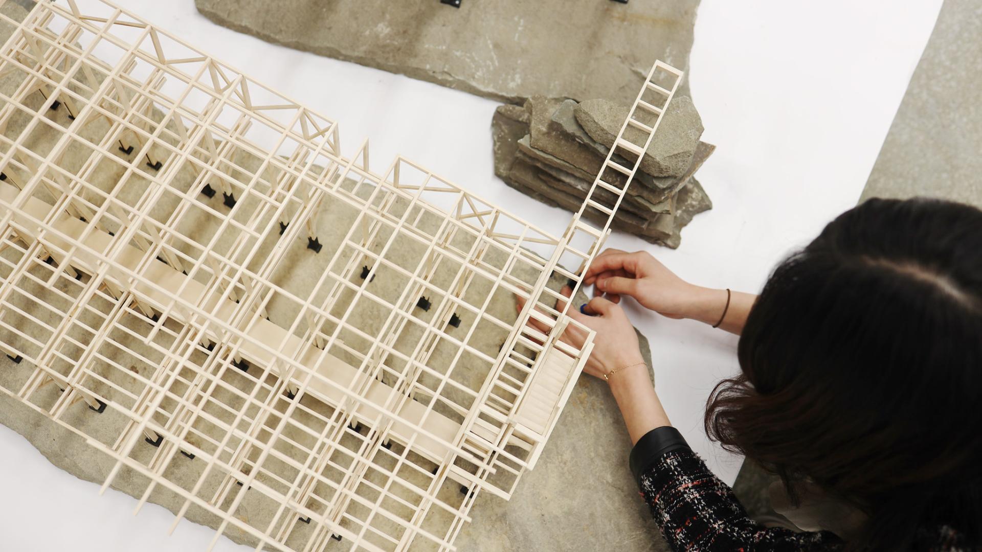 A person building a wooden architectural model.