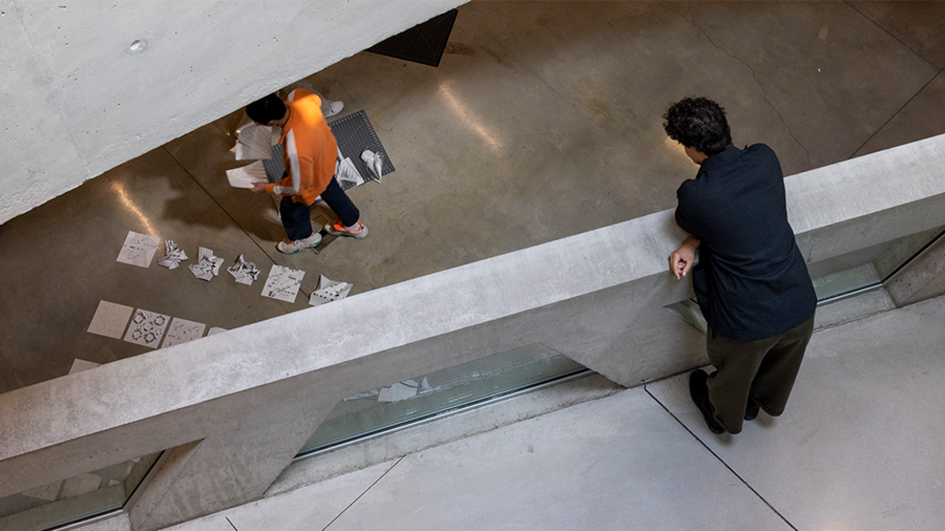 a person bending over standing on top of a bridge observing a someone else below them