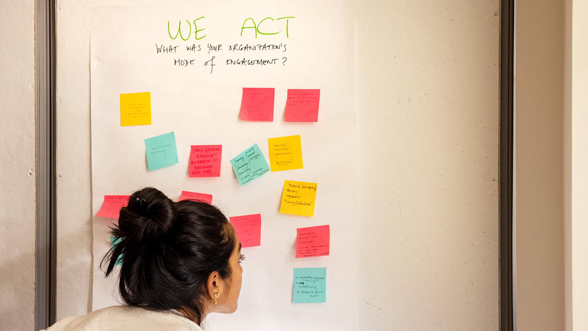 a person observing colorful sticky notes on a white poster on the wall