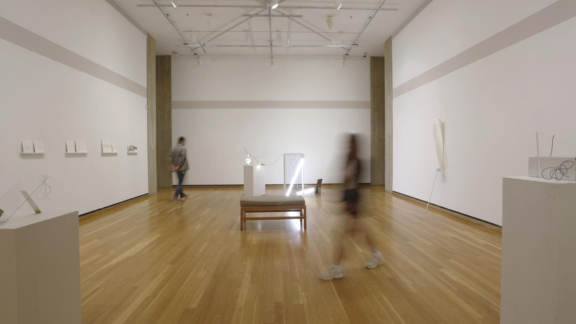 A person in a gallery with light wood flooring and white walls.