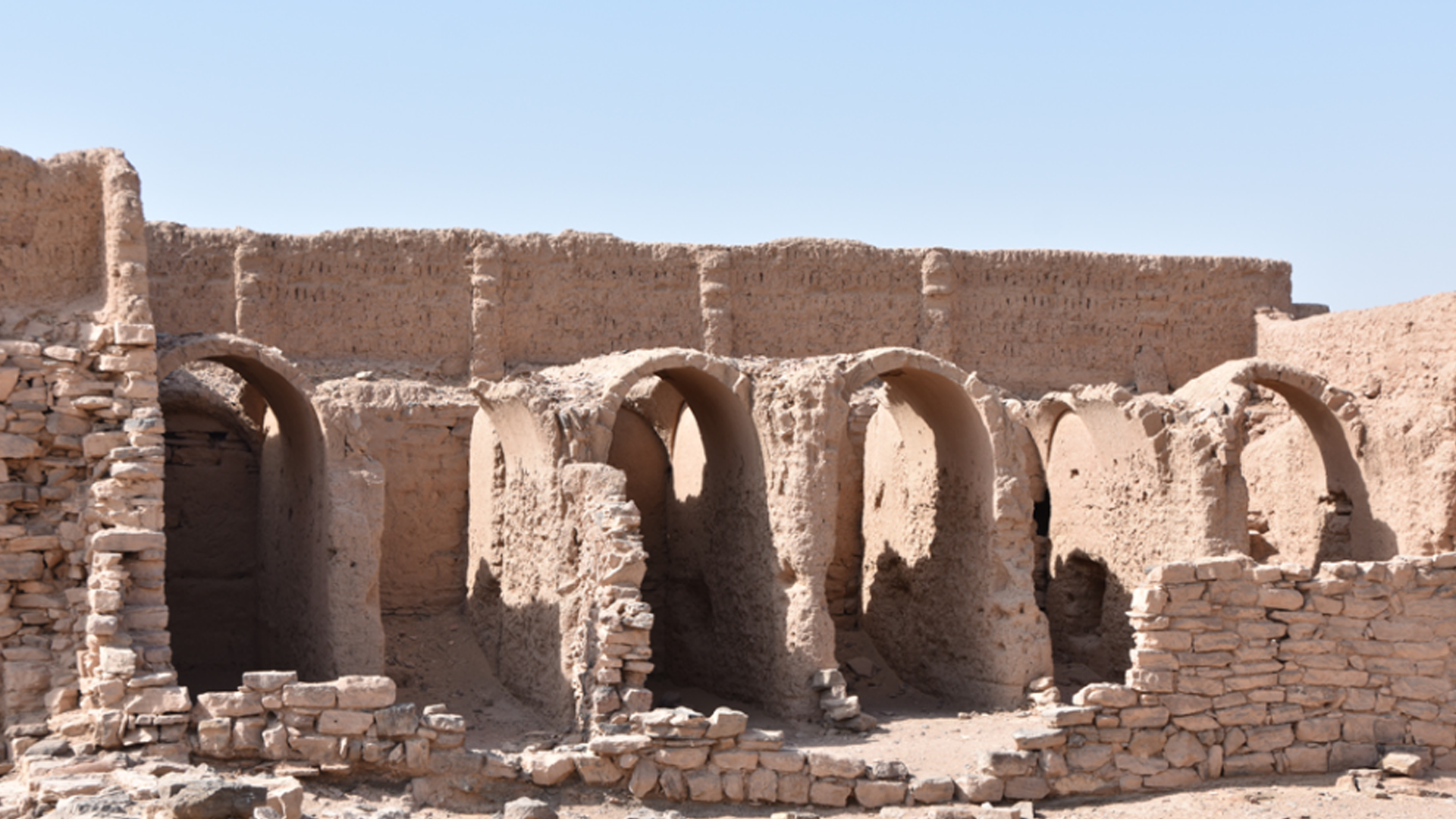 Stone and sand-like structures with round archways with a bright blue sky in the background.