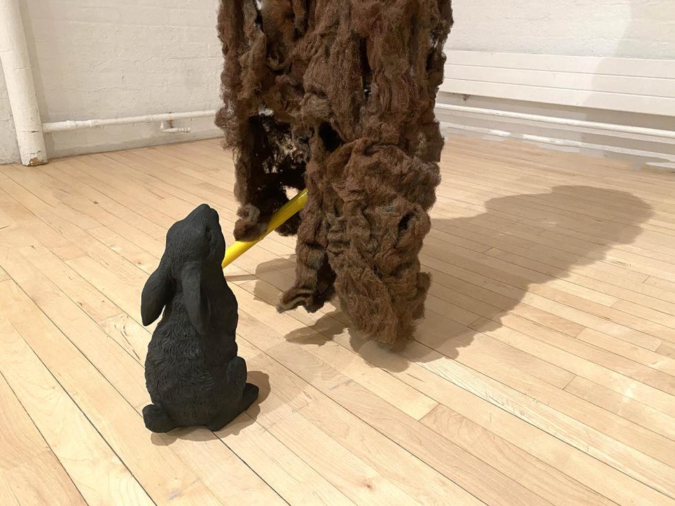 Abstract brown steel wool figure with a dark brown rabbit looking up at it.