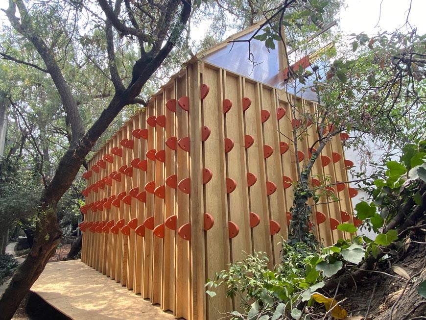 Wooden pavilion in an outdoor setting which contains protruding red / rounded elements. 