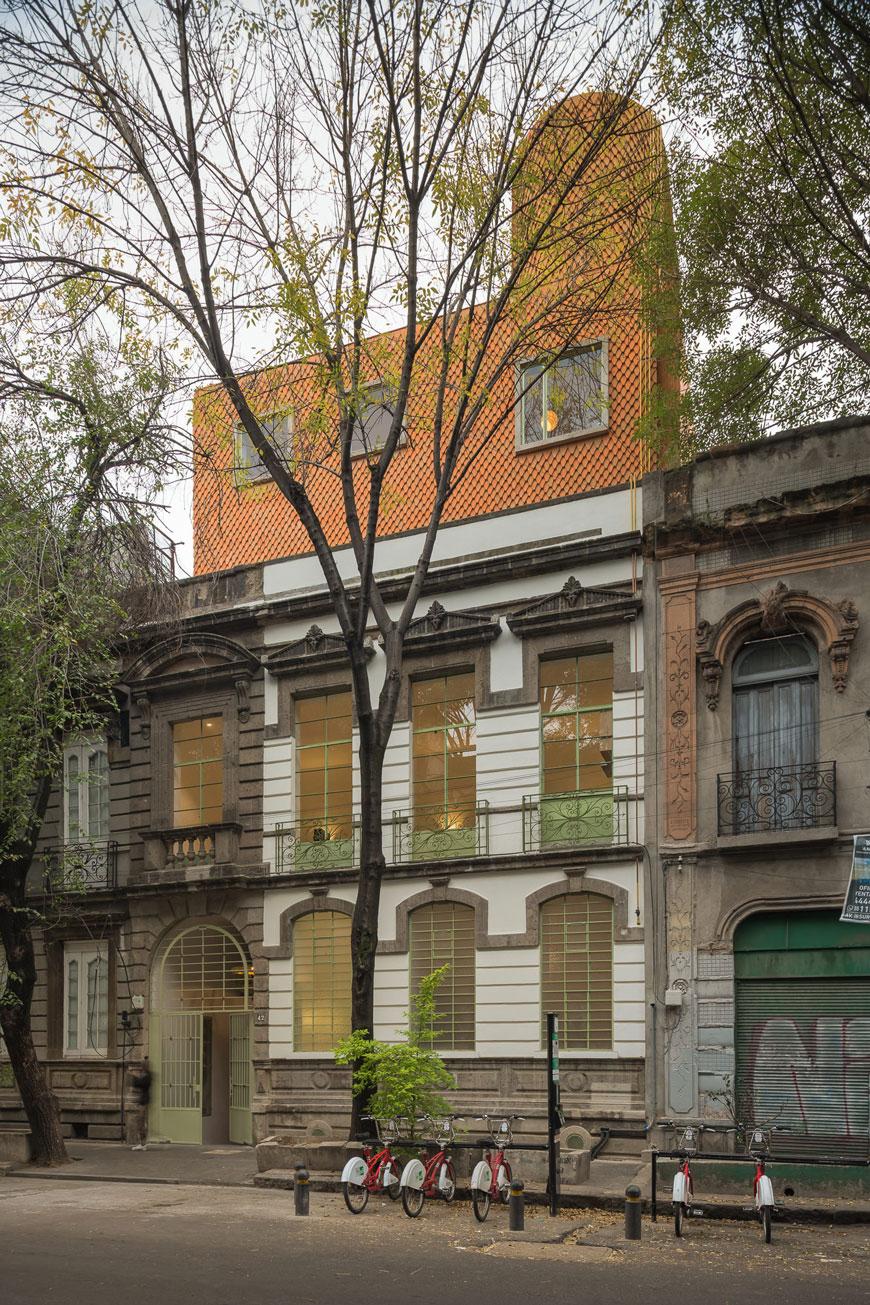 Exterior view of a 2 story home in a city setting, whose top has been expanded and adapted to contain three floors. The extention has three windows and consists of a red brick overlay. 