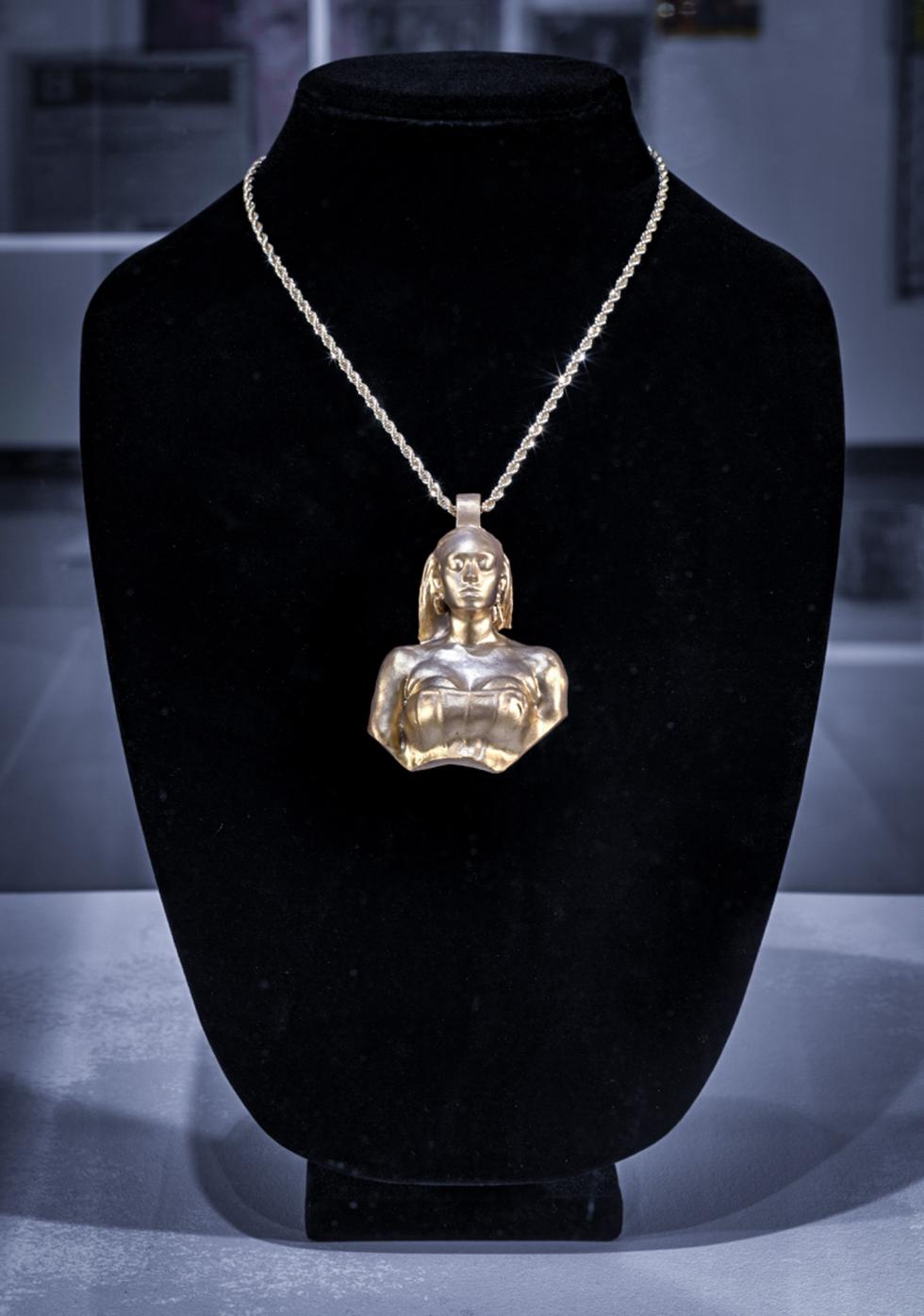 A gold pendant of a woman's bust is hung on a black velvet jewelry display