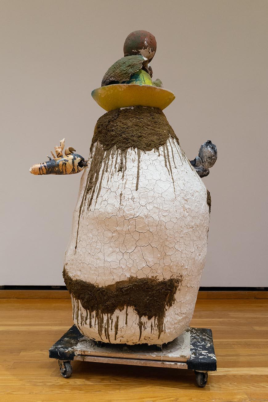 Abstract sculpture with different vegetables on top of a white boulder with dirt dripping down.