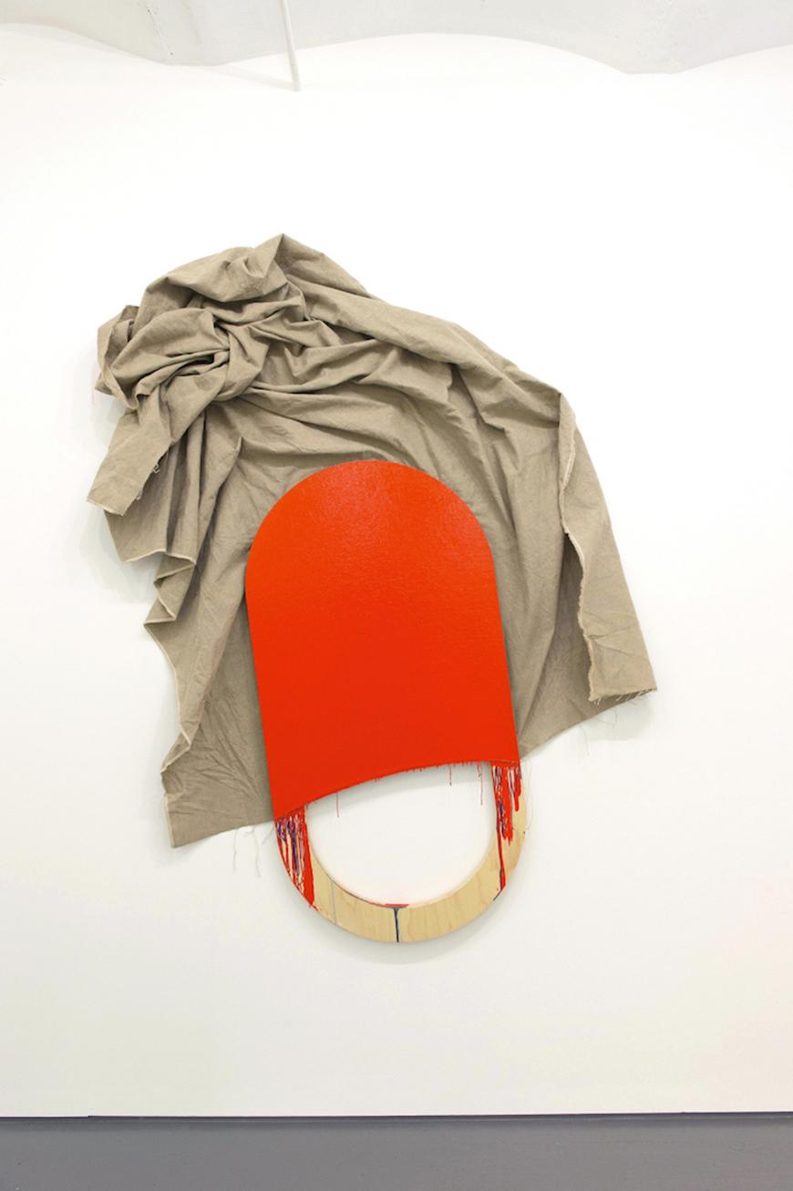 Tan fabric bunched up on a wall, partly hung behind an orange painted wooden abstract paddle.