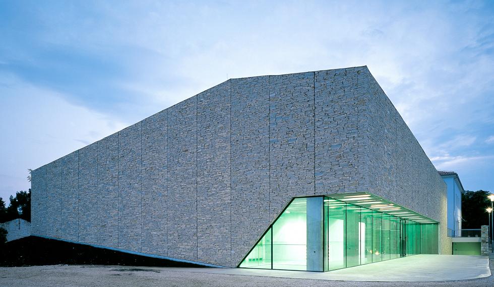 A contemporary stone-clad building with a wall of windows lit from within