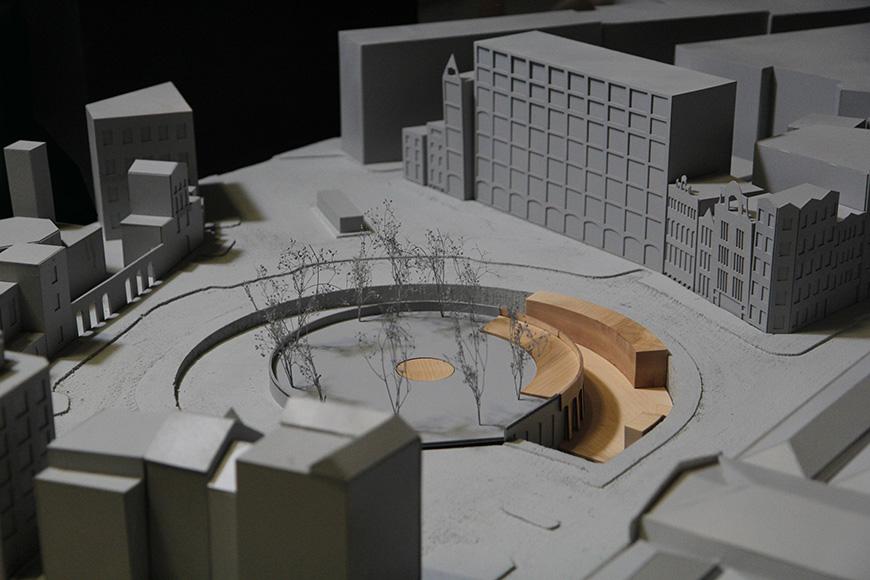 An architectural model with a round courtyard at its center surrounded by trees. 