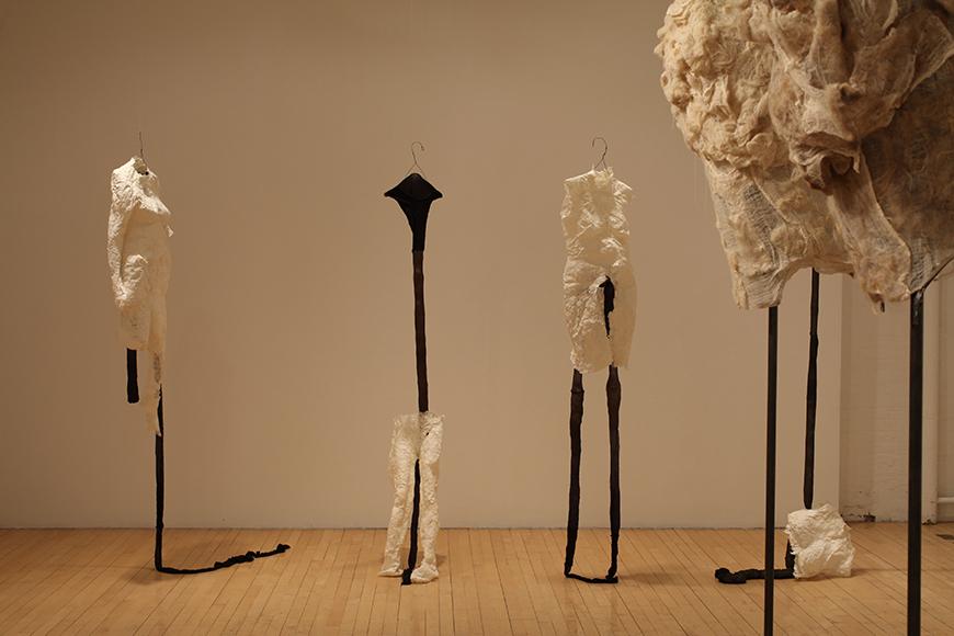 White fabric sculpture pieces placed on tall black clothes hangers.