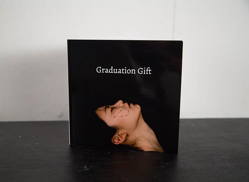 Image of a book titled 'Graduation Gift' with a woman's face looking up featuring markings on her face.