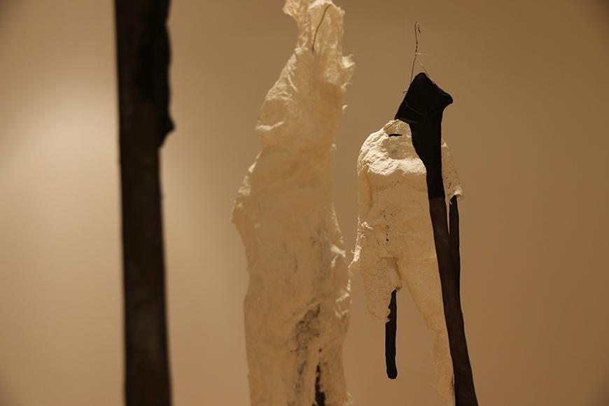 White fabric sculpture pieces placed on tall black clothes hangers.