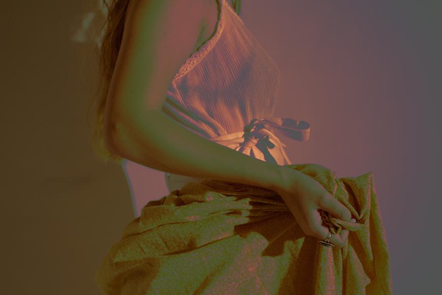 Photograph of a woman holding a piece of fabric in front of her dress in dusty rose tones.