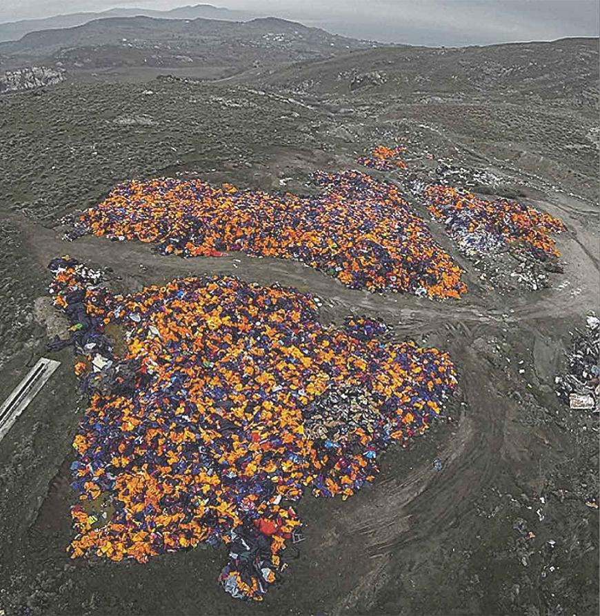 Color photograph of discarded life jackets on landfill-like dark mounds of dirt.