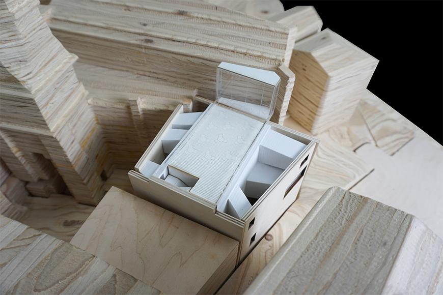 Photograph of previous model inserted into site model cut from stacked plywood, seen from aerial perspective.