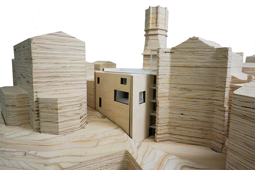 Photograph of previous model inserted into site model cut from stacked plywood, seen from the side.