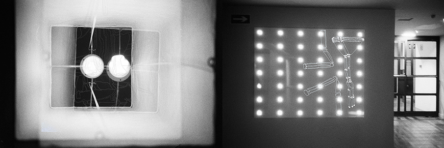 Black and white horizontal photograph of multiple lightbulbs. On the left, a fuzzy white square surrounds two large white illuminated bulbs; on the left,  a grey background sits behind a grid of 7x6 smaller illuminated lightbulbs