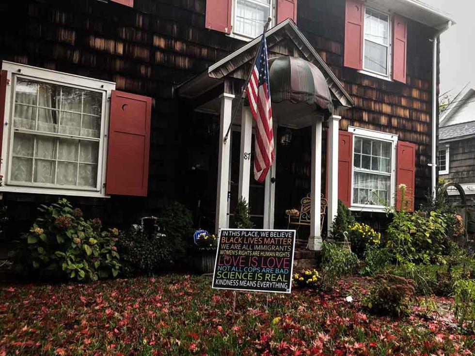 Colorful lawn sign in front of a dark brown house with an American flag out front.