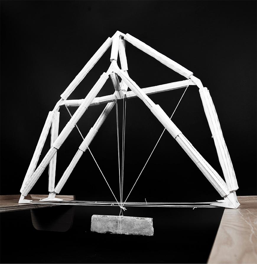 Model of a pyramid shape paper beam showcasing its strength while a brick hangs from the middle. 