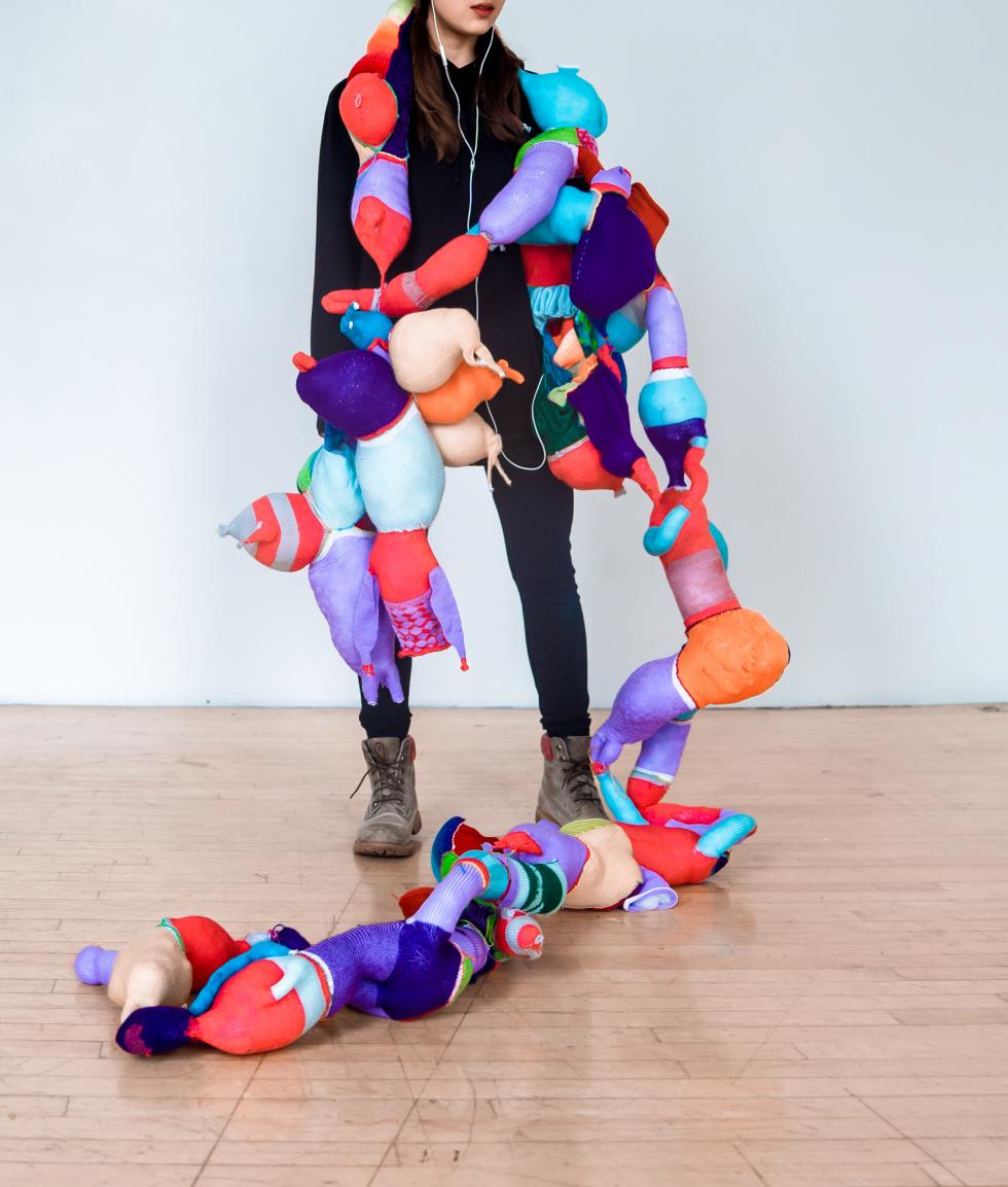 Colorful abstract shapes sewn together, draped across a woman wearing black clothes and gray boots.