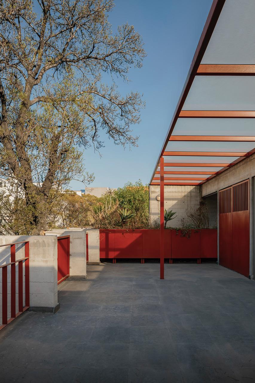 A building featuring red railings, surrounded by trees and under a clear sky. The area is empty, showcasing the architecture and floor of the property.