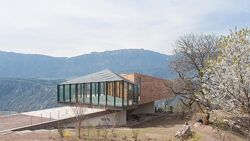 Building with an enclosed glass front space with an inclined walk leading up to it.