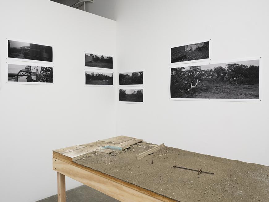 A long wooden table with eight black and white photographs on the wall surrounding it.