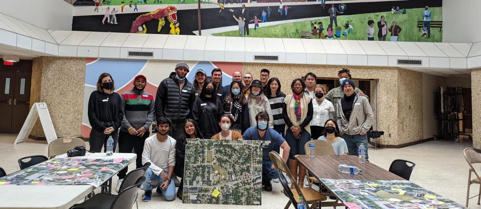 class, teacher and project partners posing with city plans indoors with tables and chairs