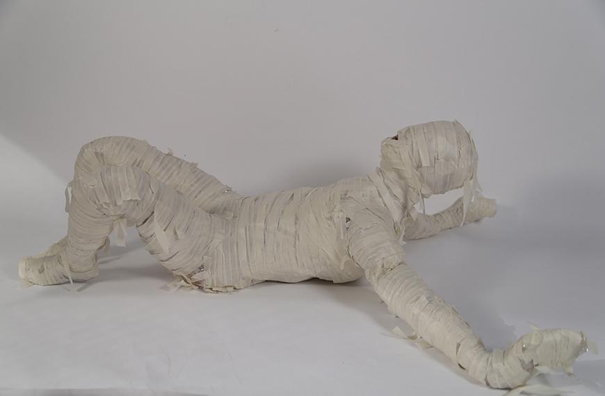 sculpture of a person lying on the ground wrapped in masking tape.