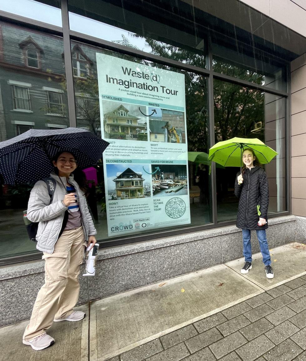 Students holding umbrellas and posing in front of a very large poster for the 