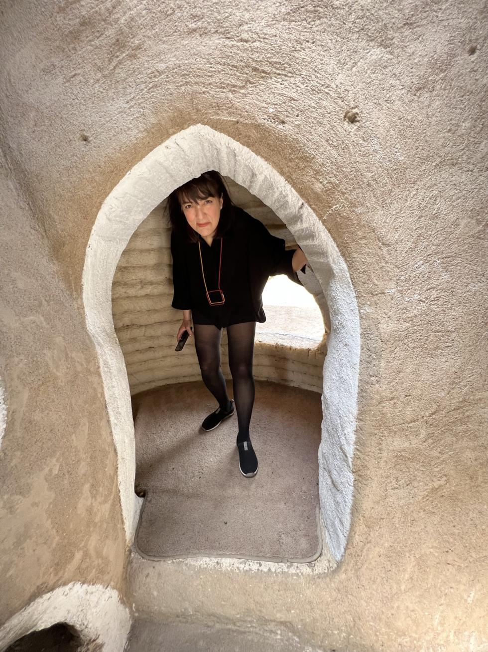 A woman dressed in all black ducking down as she walks through a tunnel.
