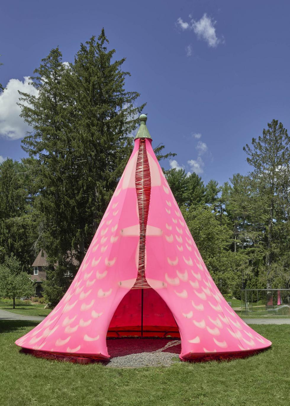 Cone-shaped pink tent with light yellow designs, trees and a blue sky in the background.